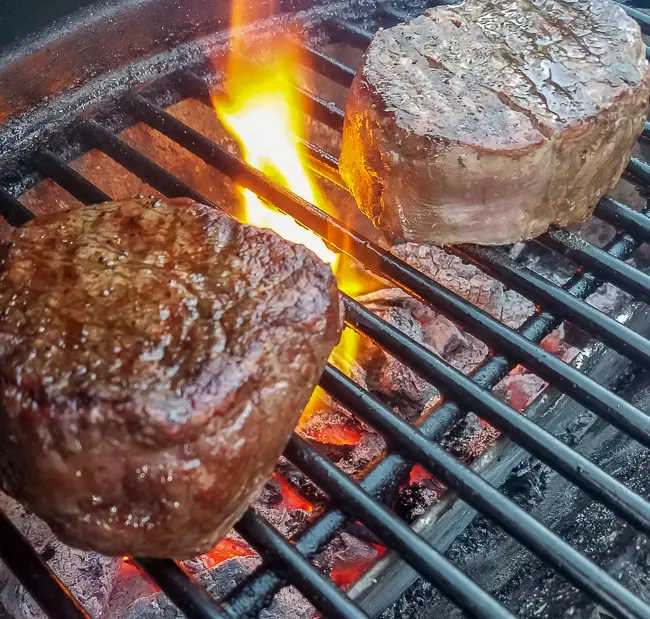 Tenderloin steaks on a grill with a flame beside the steak.