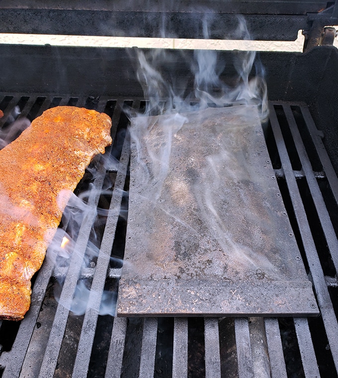 stainless steel pouch of wood chips on a gas grill smoking beside ribs