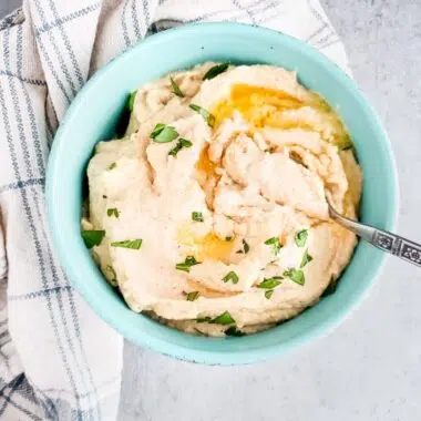 Mashed cauliflower with melted butter and parsley in a blue bowl.