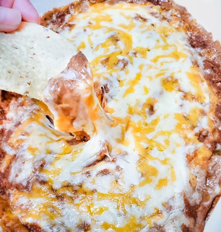 Dipping a chip in baked bean dip with melted cheese on top.