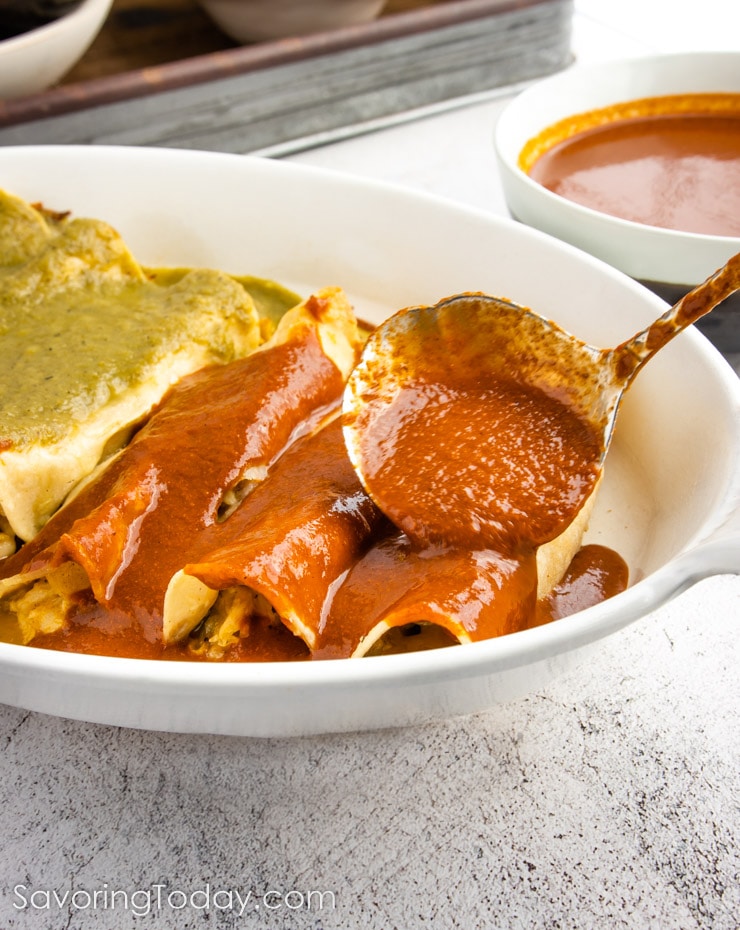 Red chile enchilada sauce spooned over enchiladas in a white dish.