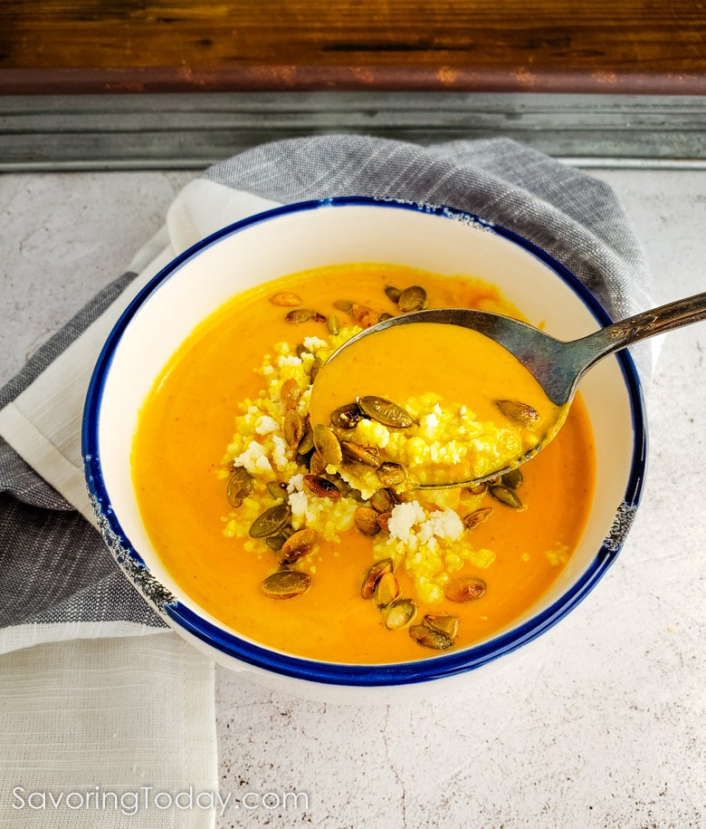 a spoonful of pumpkin soup with cotija cheese and pepitas on top