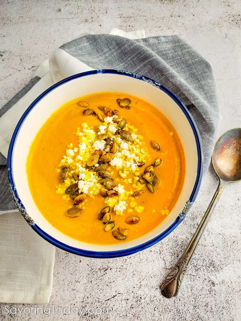 Pumpkin soup in a white bowl topped with cotija cheese and toasted pepitas.