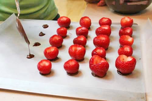 Hulled strawberries on chocolate set on wax paper for filling with cheesecake.