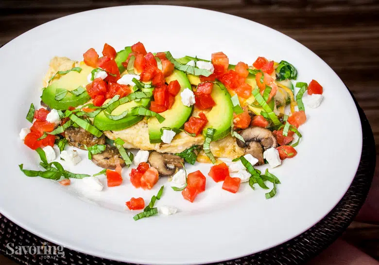 spinach and mushroom omelet on a white plate with tomatoes and avocado