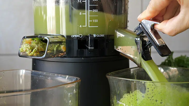 green juice pouring out of juicer on one side with pulp on the other 