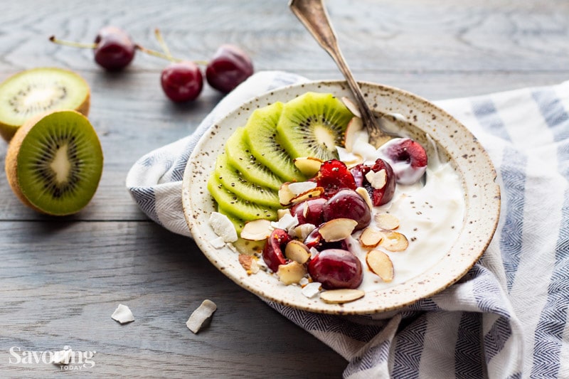 bowl with yogurt topped with cherries and kiwi on a wood table