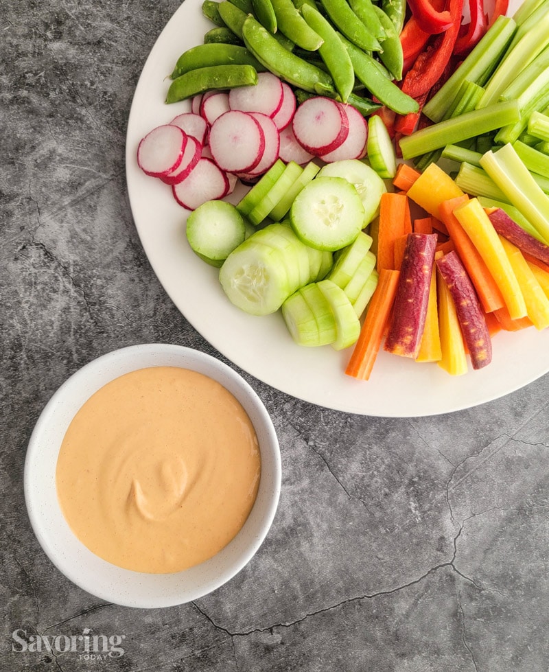 cut vegetables on a white platter beside a bowl of dip