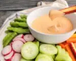 A carrot scooping up dip surrounded by veggies.