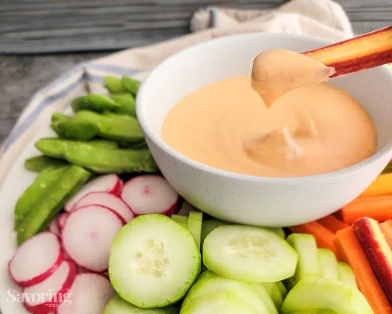 A carrot scooping up dip surrounded by veggies.