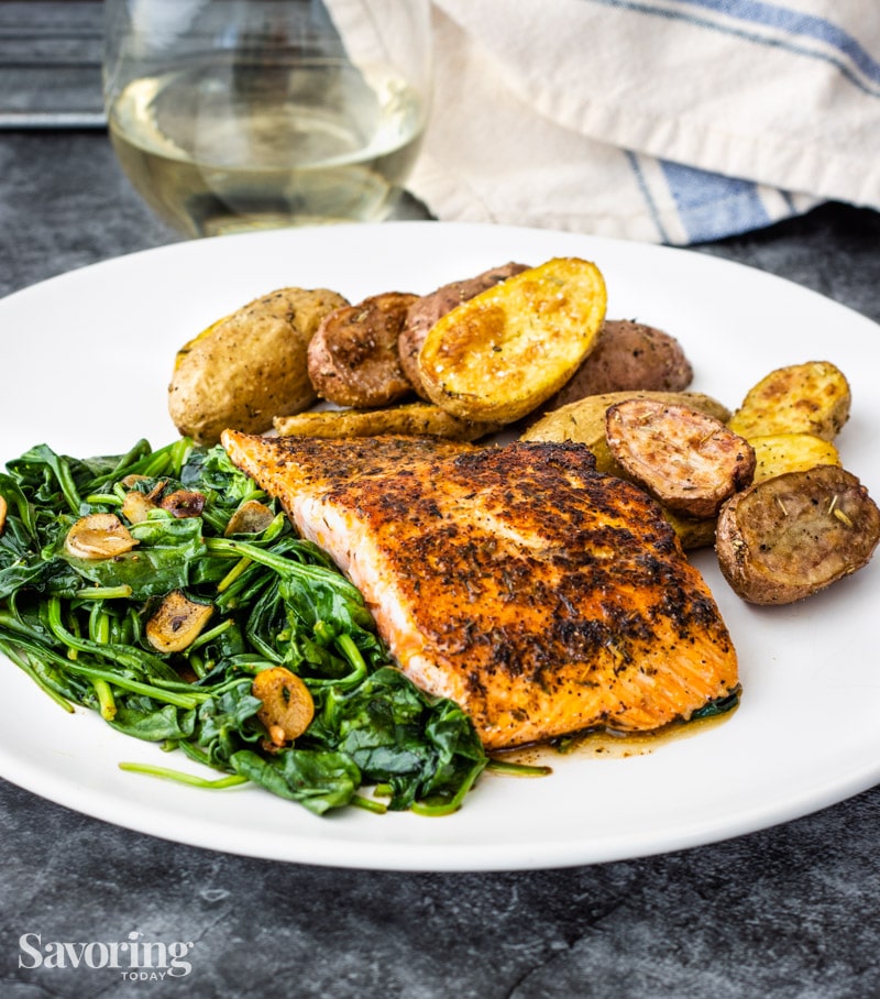 Blackened salmon on a white plate with spinach and potatoes