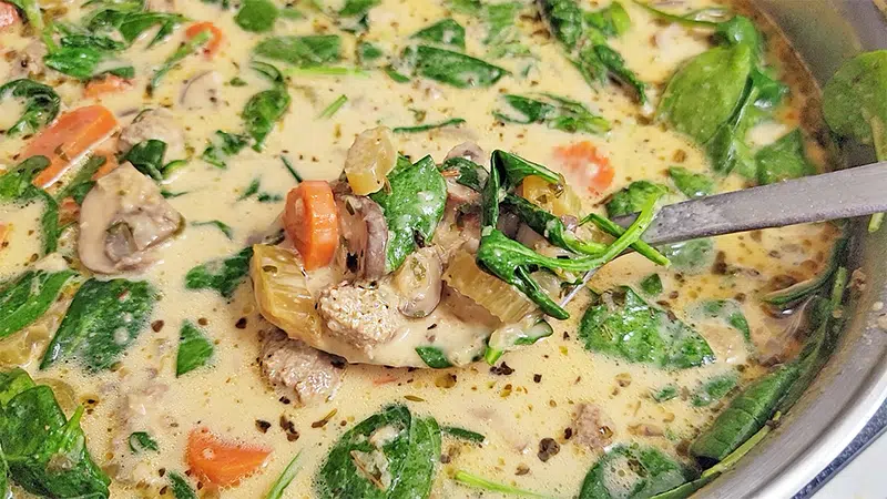 creamy soup with meatballs, carrots, celery and spinach in a pot