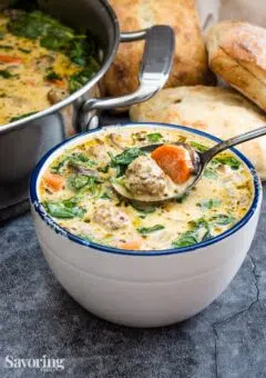 Meatball soup in a white bowl with a spoonful out of the bowl