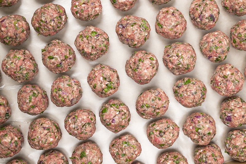 Rows of raw homemade meatballs prepared for cooking on a tray, overhead view