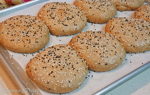 wheat buns on a sheet pan sprinkled with sesame seeds ready for the oven 