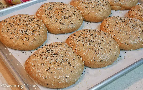 wheat buns on a sheet pan sprinkled with sesame seeds ready for the oven 