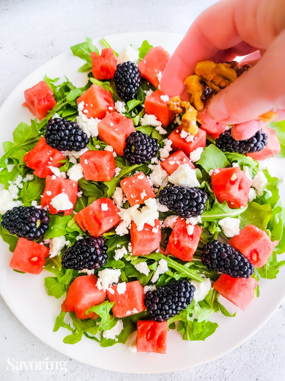 Adding walnuts to a sald with arugula, watermelon, blackberries and feta