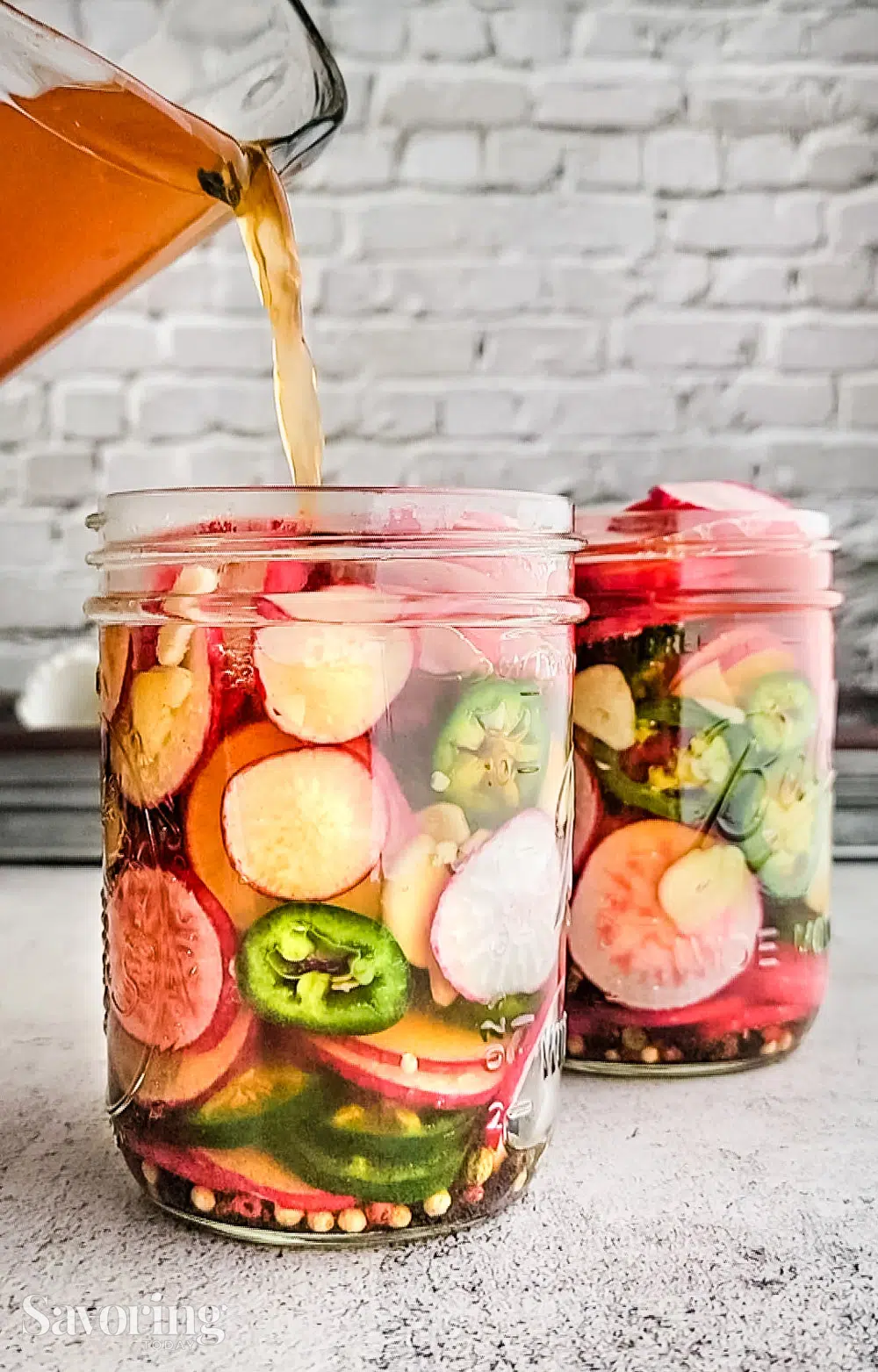 pouring brine over jalapenos and radishes in a pint jar