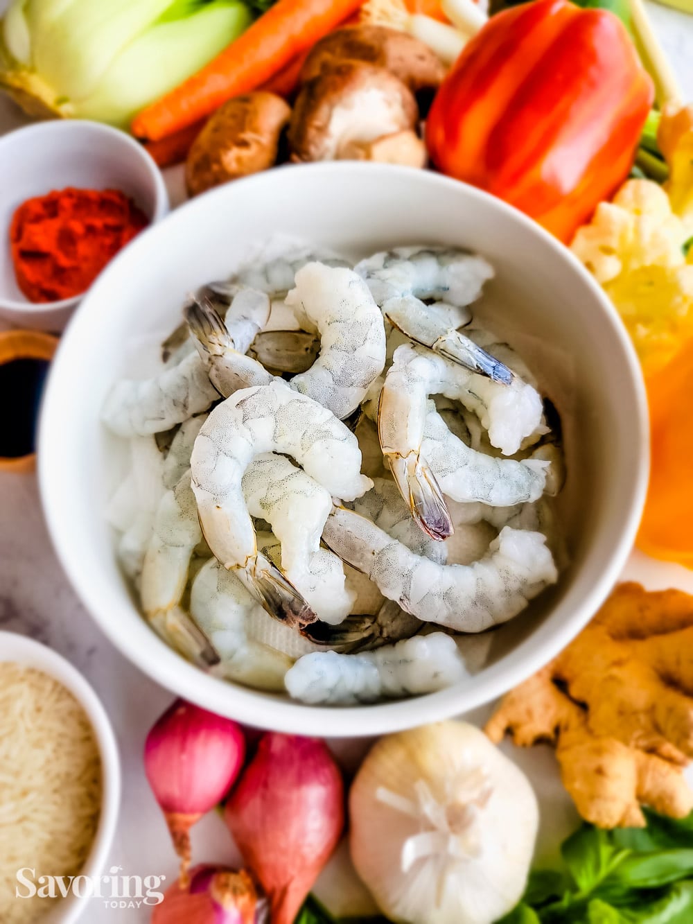 peeled shrimp in a white bowl in the middles of vegetables on a counter