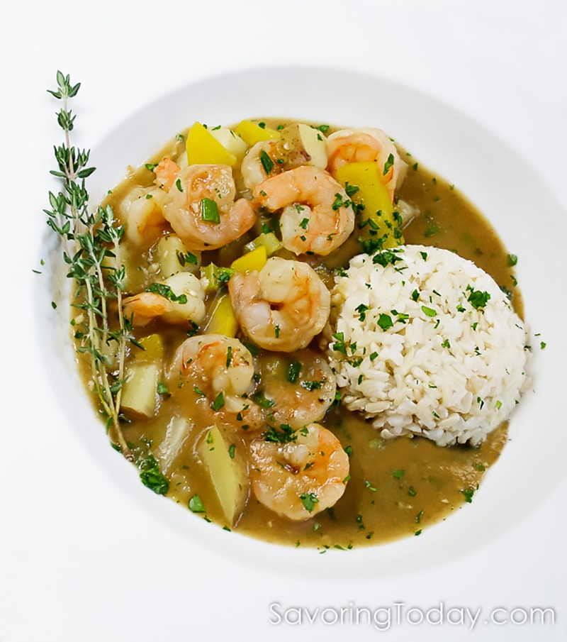 Shrimp and potatoes in a rich gravy with rice in a white bowl.