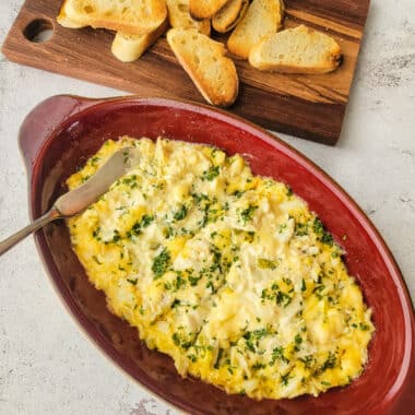 Crab and gouda dip in a red dish with sliced bread toast