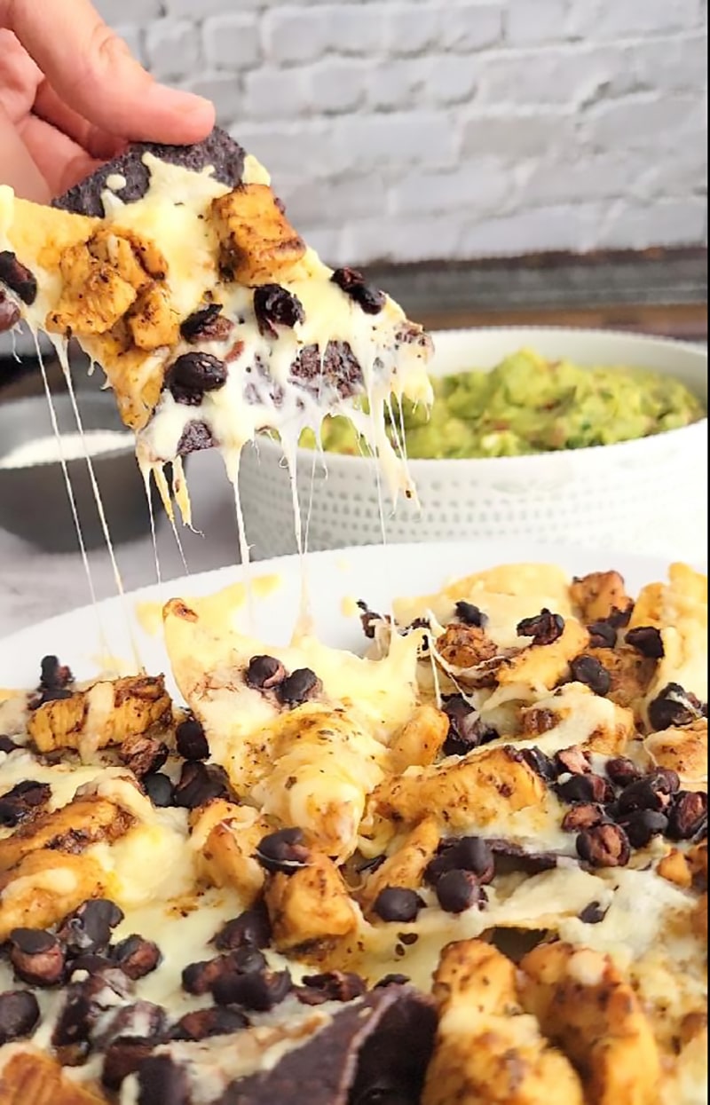 Chicken and black bean nachos on a plate with some being pulled away