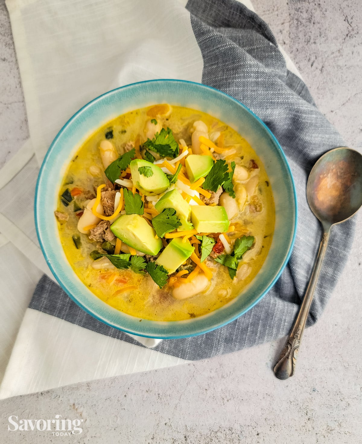 white turkey chili in a blue bowl with avocado, cheese, and cilantro on top