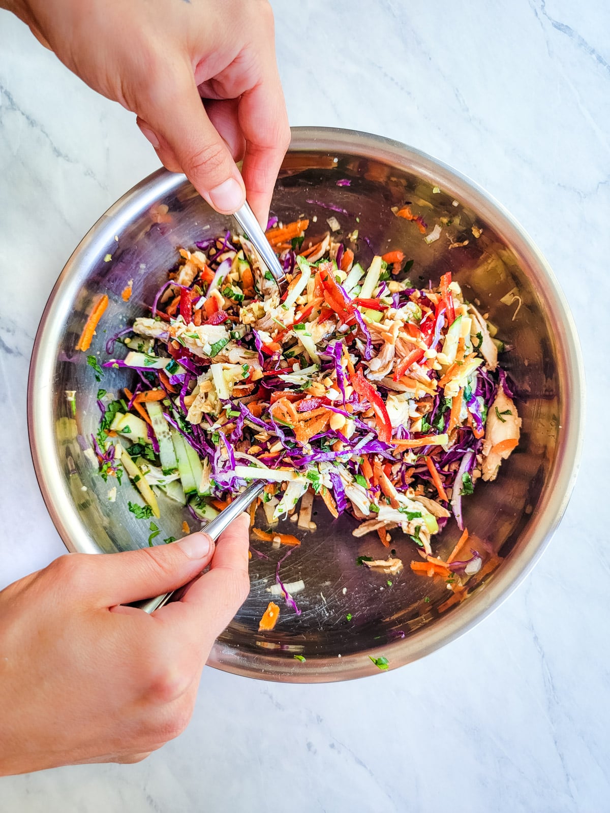 Tossing salad ingredients with two spoons in a metal bowl