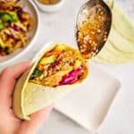 Spooning dressing onto a handheld chicken wrap when serving