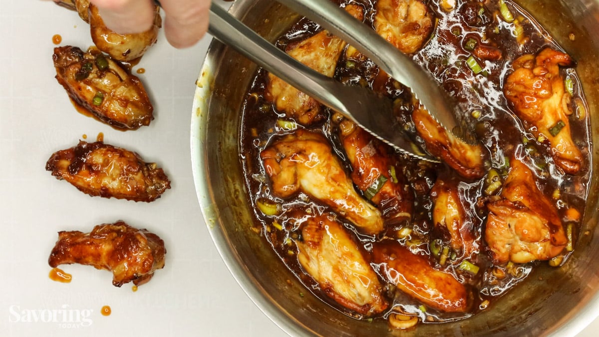 Dipping chicken wings into sauce with tongs