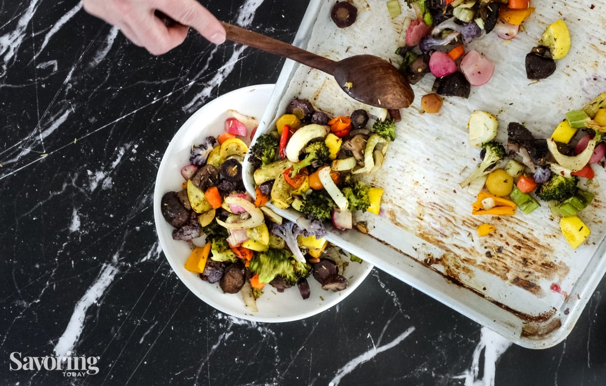 scraping roasted vegetables off a sheetpan into a bowl