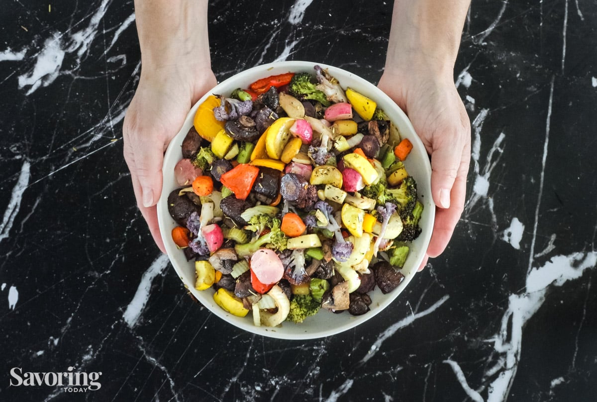 hands holding a bowl of roasted vegetables