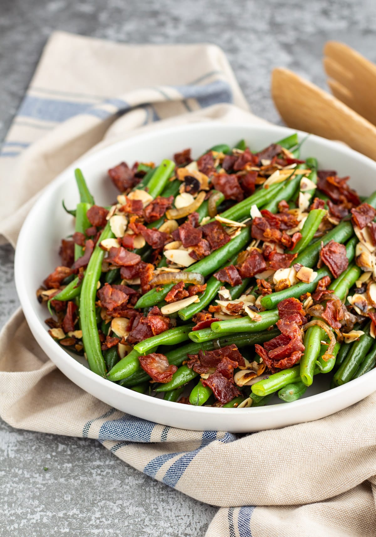 green beans with almonds and crisp prosciutto in a white bowl on a towel