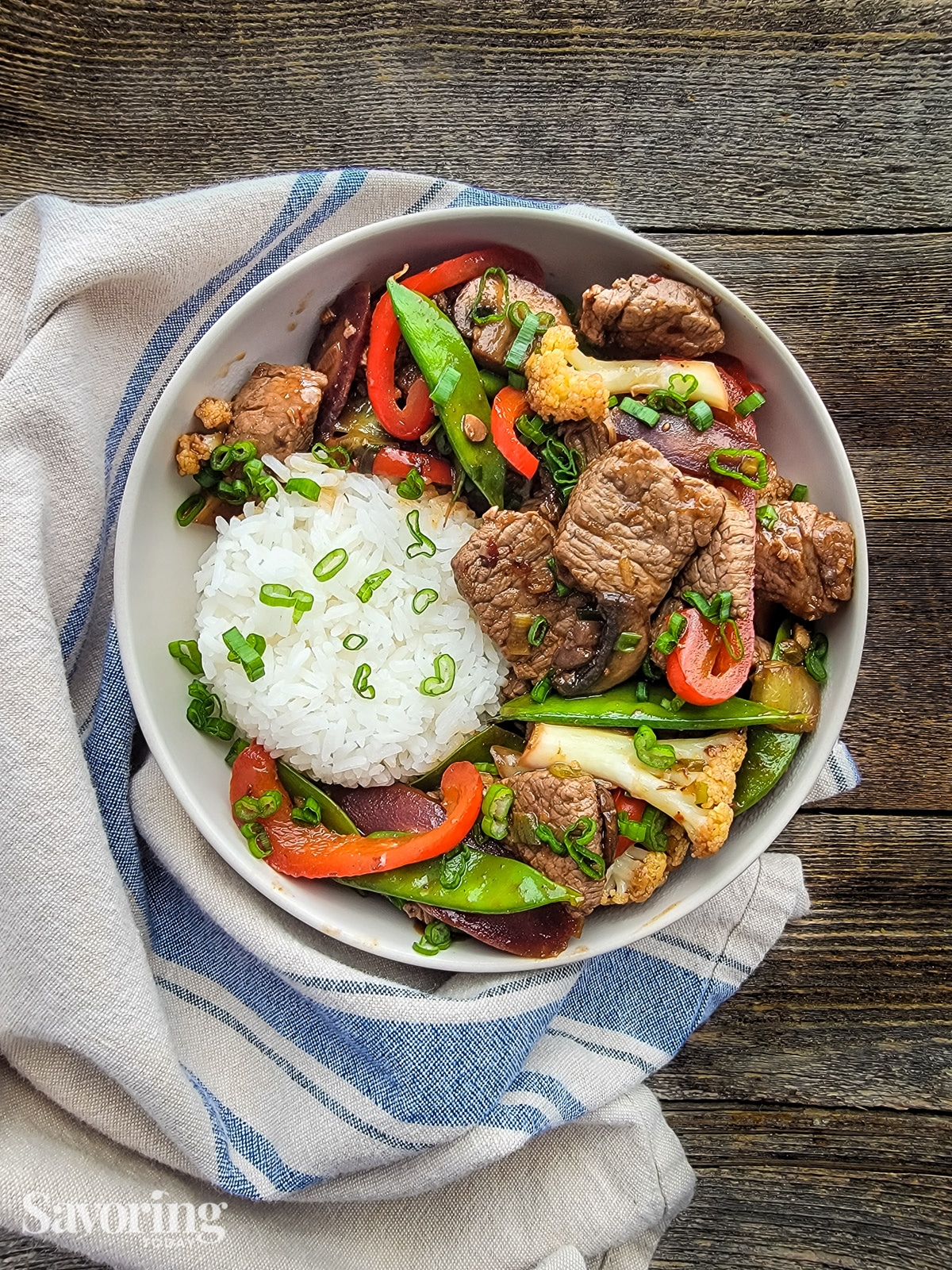 Stir-fry beef and vegetables in a brown sauce served with rice in a white bowl