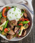 Mongolian beef and vegetables served with rice in a white bowl