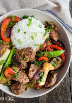 Mongolian beef and vegetables served with rice in a white bowl