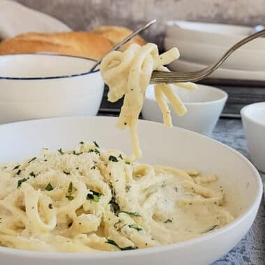 lemon alfredo on a fork held above the bowl