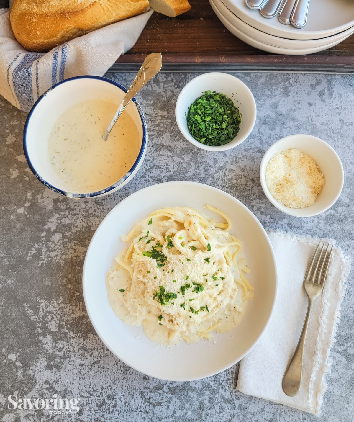 Alfredo over pasta on a table with side bowls of parsley and cheese