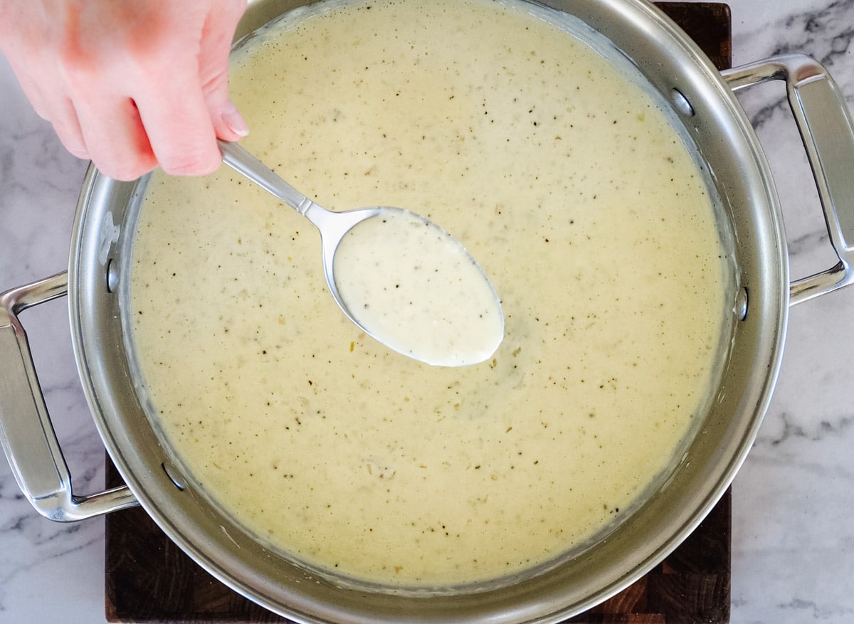 a spoonful of alfredo sauce held over a pan
