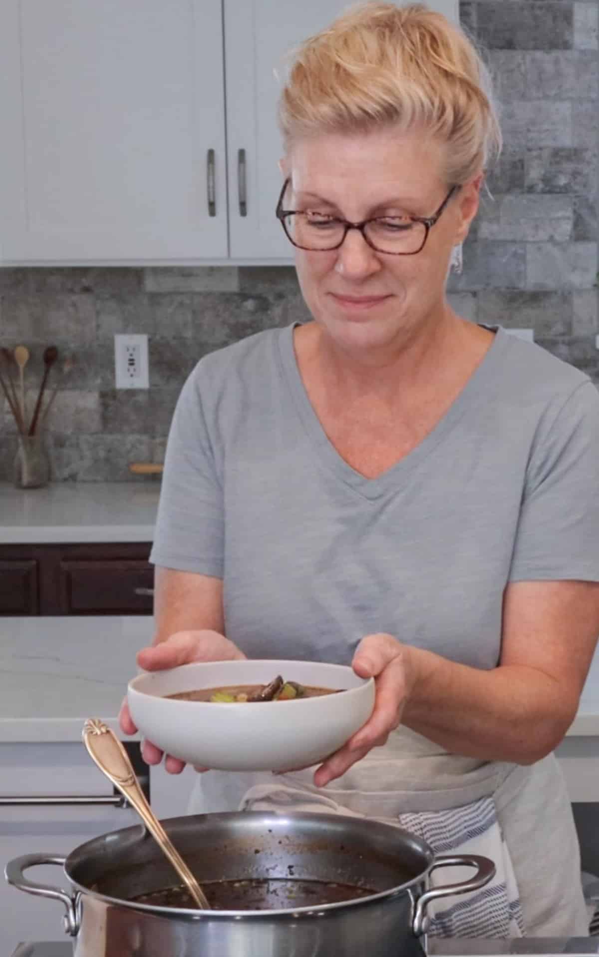person holding a bowl of vegetable beef barley soup above the pot 