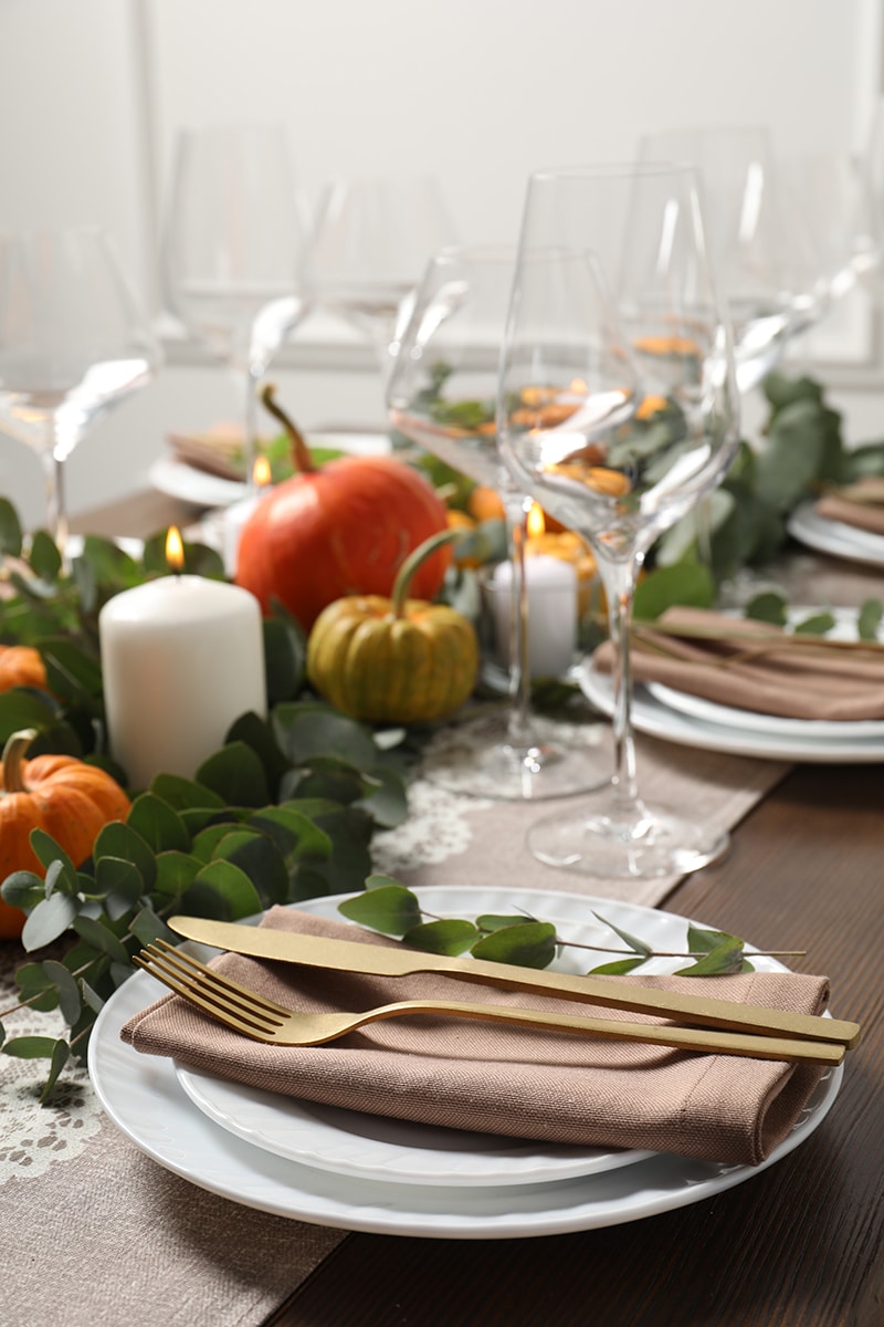 tablescape with pumpkins, candles, wine glasses and brown napkins on white plates