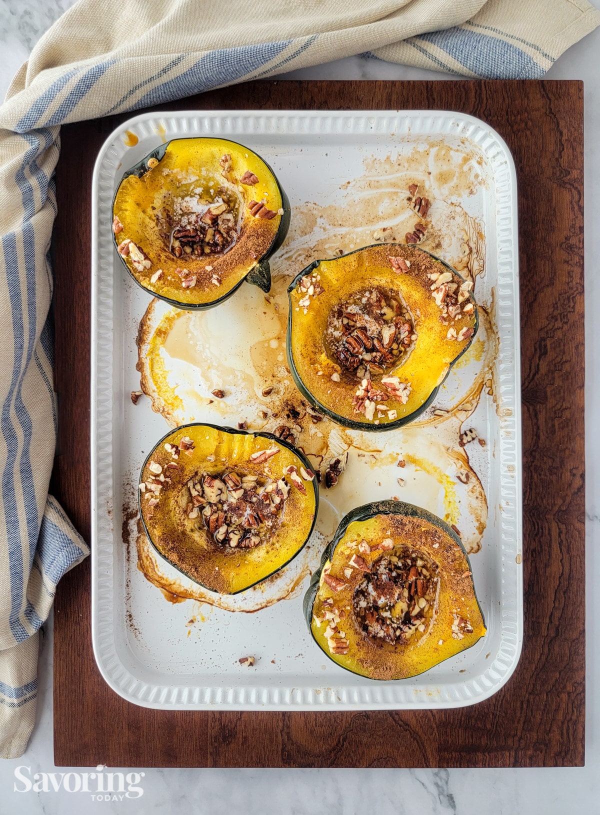 Roasted acorn squash topped with pecans in a baking dish on a cutting board