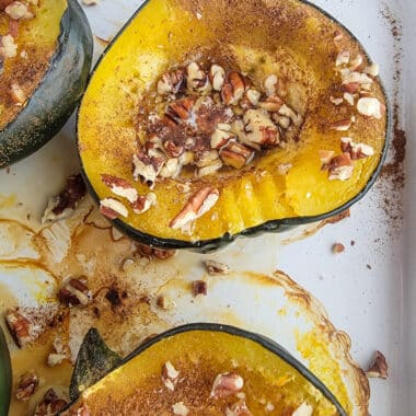 Roasted Acorn squash on a white baking dish topped with pecans