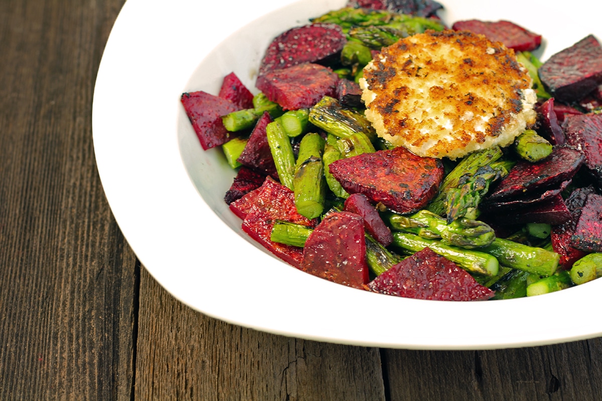grilled beets and asparagus in a white bowl with a disc of fried goat cheese on top