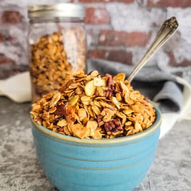 Golden brown granola in a blue bowl with spoon in front of a jar of granola