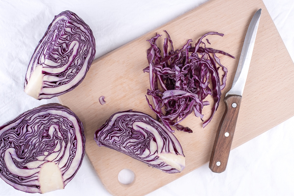 Red cabbage sliced thin on a cutting board with a knife