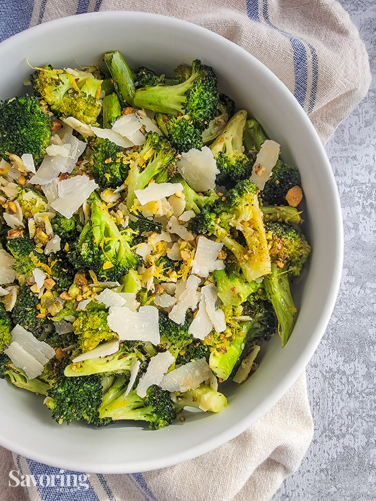 roasted broccoli with shaved parmesan, lemon zest, and pistachios in a white bowl set over a towel