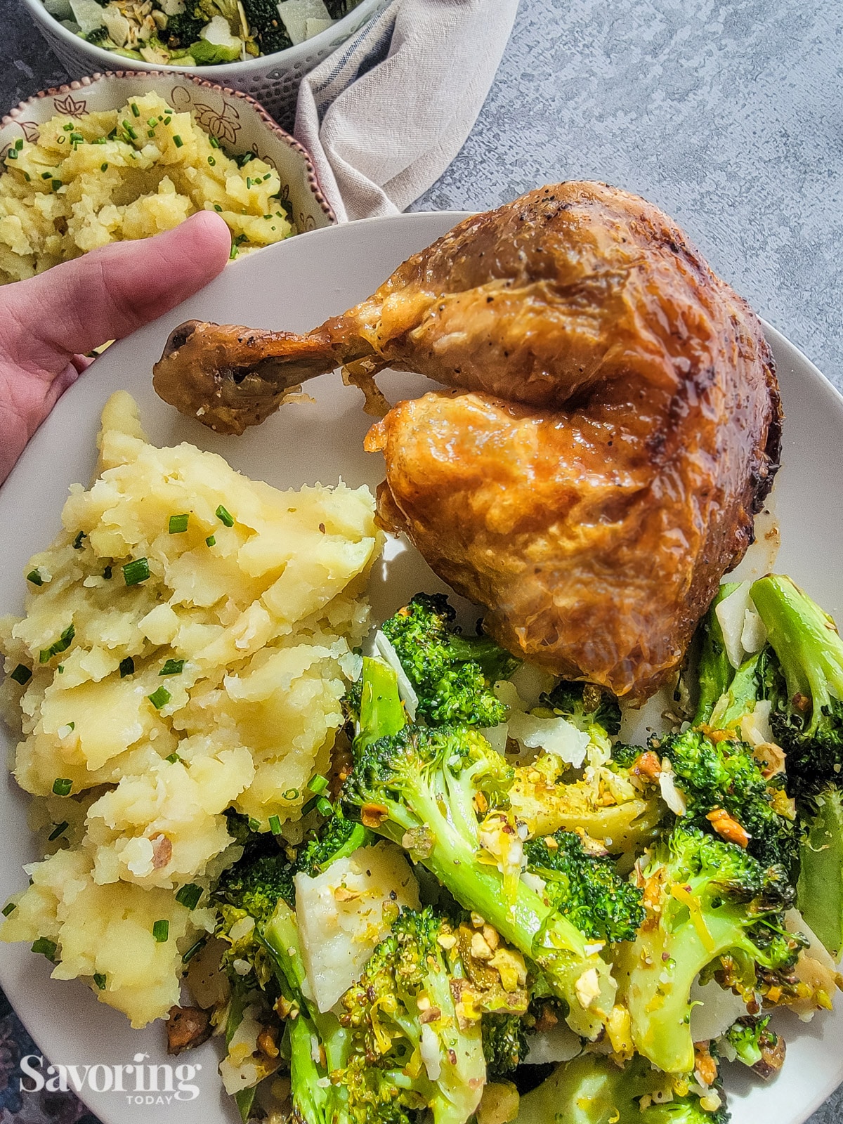 A hand holding a plate of roasted chicken, broccoli, and mashed sweet potatoes
