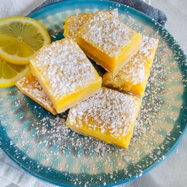 Lemon bars on a blue plate with powdered sugar on top