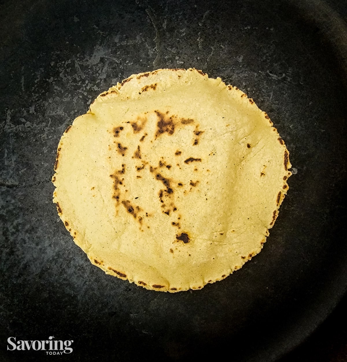 A cooked corn tortilla on a black cast iron skillet